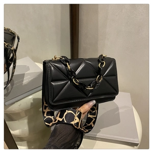 Close-up of black quilted shoulder bag with chain handle and woven geometric strap