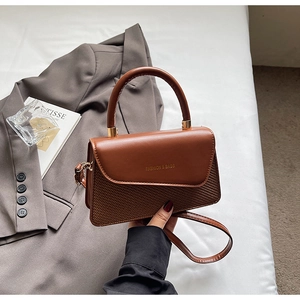 Detail of a brown leather crossbody bag with woven texture and gold fashion lettering