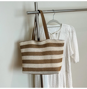 Detail view of woven striped tote bag featuring brown leather shoulder straps and straw texture