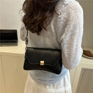 Elegante borsa a spalla in pelle nera con fibbia dorata indossata da una modella
