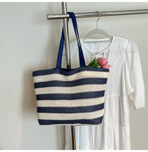 Straw woven tote bag with navy stripes hung against a white lace dress backdrop