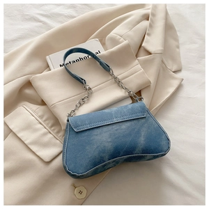 Detail of blue denim shoulder bag featuring a vintage metal chain and curved flap design