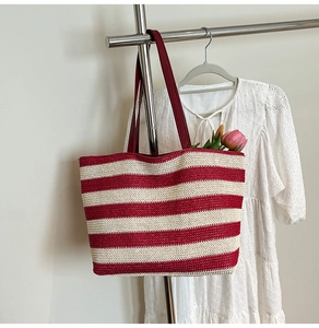 Detailed view of large striped woven tote bag with red shoulder straps and a floral detail
