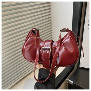Detail of dark red crescent shoulder bag featuring glossy patent leather and buckle strap