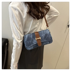 Détail du sac à bandoulière en denim bleu marine avec sangle en cuir brun et boucle