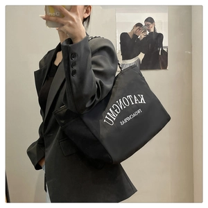 Close-up of black tote bag featuring white lettering and decorative metal chain straps
