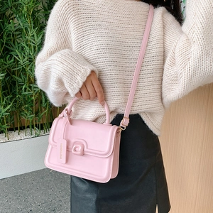 Pink faux leather crossbody bag with flap and metal buckle in a natural indoor setting