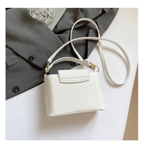 Detail of white textured leather handbag with gold metal clasp on a grey blazer