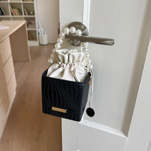Detail of elegant bucket bag with large pearl handle and woven texture on a door handle