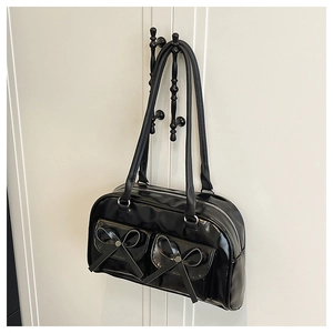 Detail of black glossy PU bag with bow accents and silver rivets on a white door