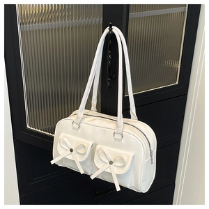 Detail of white Boston bag with bow accents and glossy leather texture on a minimalist handle