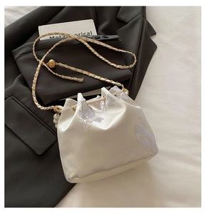 Close-up of floral embroidery on pearl bucket bag with gold chain and silk fabric
