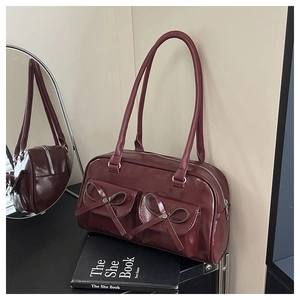 Detail view of burgundy glossy Boston bag with leather bows and dual front pockets