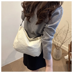 Side view of cream nylon dumpling bag with black strap worn by a model