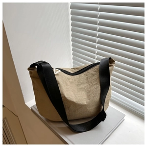 Detail of khaki nylon dumpling bag with black strap and zipper on a decorative book