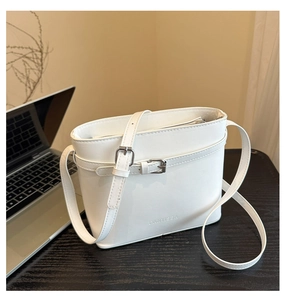 Close-up of white minimalist bucket bag with adjustable strap and silver buckle on desk