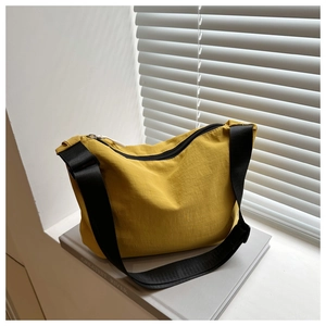 Detail of yellow nylon crossbody bag with black zipper and strap on books in sunlight