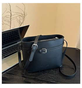Detail of minimalist black leather bucket bag featuring debossed logo and silver buckle