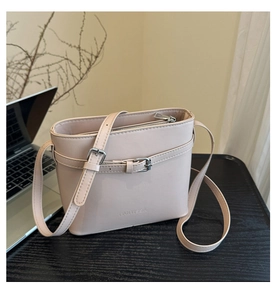 Detailed view of beige bucket bag with FANYISSA logo and decorative buckle on wood surface