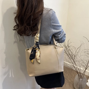 Classic beige tote bag with a decorative silk scarf on the strap shown in lifestyle scene