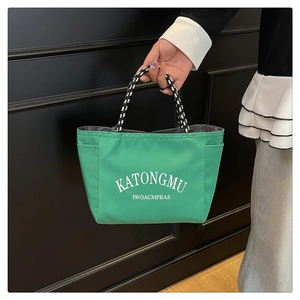 Detail of green nylon tote bag featuring white lettering and woven monochrome handles