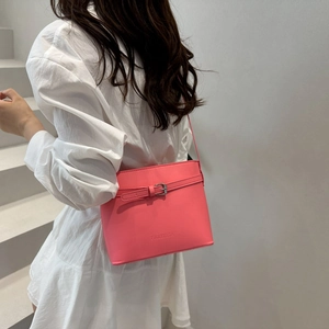 Bright pink leather bucket bag with decorative buckle shown on a model in white dress