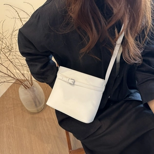 Minimalist white bucket bag with silver buckle and crossbody strap worn by a model