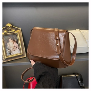 Detail of glossy brown leather shoulder bag with adjustable strap in boutique setting
