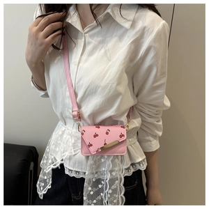 Détail d'un mini sac bandoulière rose avec imprimés cerises et accents métalliques dorés