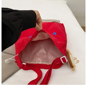 Macro detail of red large-capacity tote bag showing waterproof lining and bread pendant