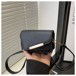 Détail d'un mini sac bandoulière noir avec une barre métallique dorée sur le rabat avant