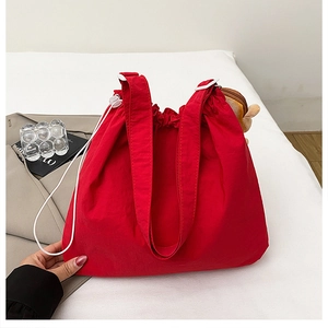 Detail of red drawstring tote bag with plush charm and wide shoulder strap