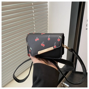 Détail du sac bandoulière noir avec imprimé cerises et garniture métallique dorée