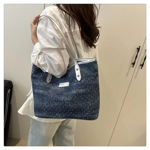 Detail view of large blue denim tote bag with silver handles worn on shoulder