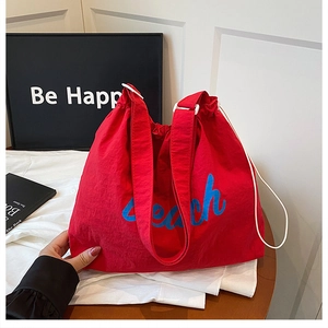 Close-up of red nylon tote bag with blue Beach lettering and adjustable shoulder strap
