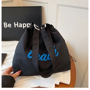 Close-up of black drawstring tote bag featuring blue Beach text and adjustable strap