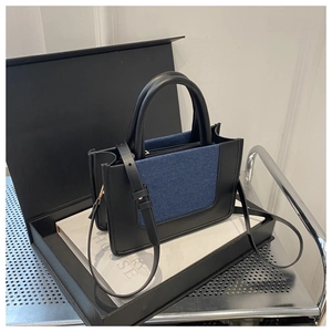 Close-up of black leather and blue denim patchwork handbag with sturdy round handle