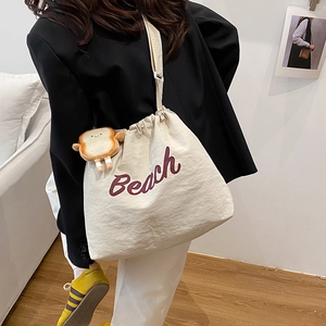Stylish cream canvas tote bag with red Beach lettering and cute toast pendant on shoulder
