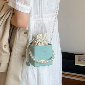 Detail of mint green bucket bag with large pearl handle and golden chain strap