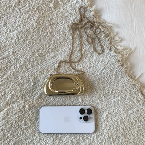 Close-up of golden pebble-shaped evening bag with metallic mirror finish and chain