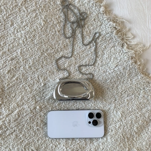 Mini silver mirror acrylic clutch bag with pearl chain shown next to a smartphone