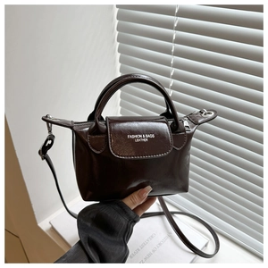 Close-up of a dark brown glossy leather dumpling bag with white fashion text and metal zipper