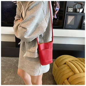 Red lychee grain leather crossbody bag shown on model in a modern interior setting