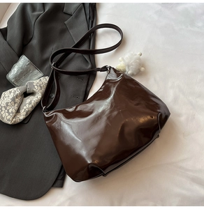Détail du sac cabas en cuir verni marron foncé avec pompon blanc et bandoulière chaîne