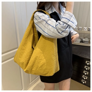 Shoulder view of large ginger yellow nylon tote bag showing draping texture and wide strap