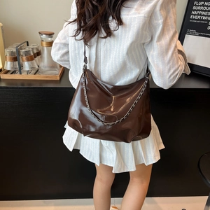 Dark brown patent leather crescent tote bag with silver chain detail worn by a model