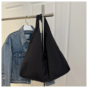 Detailed view of black nylon tote bag on hanger next to a classic denim jacket