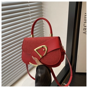 Detail of red crossbody bag showing textured fabric flap and gold D-ring buckle