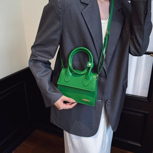 Sac à main en cuir vert avec poignée ronde et logo doré sur un costume gris