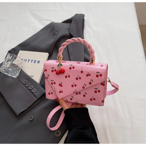 Gros plan détaillé d'un sac à main rose à motif cerises avec charm cerise 3D et poignée